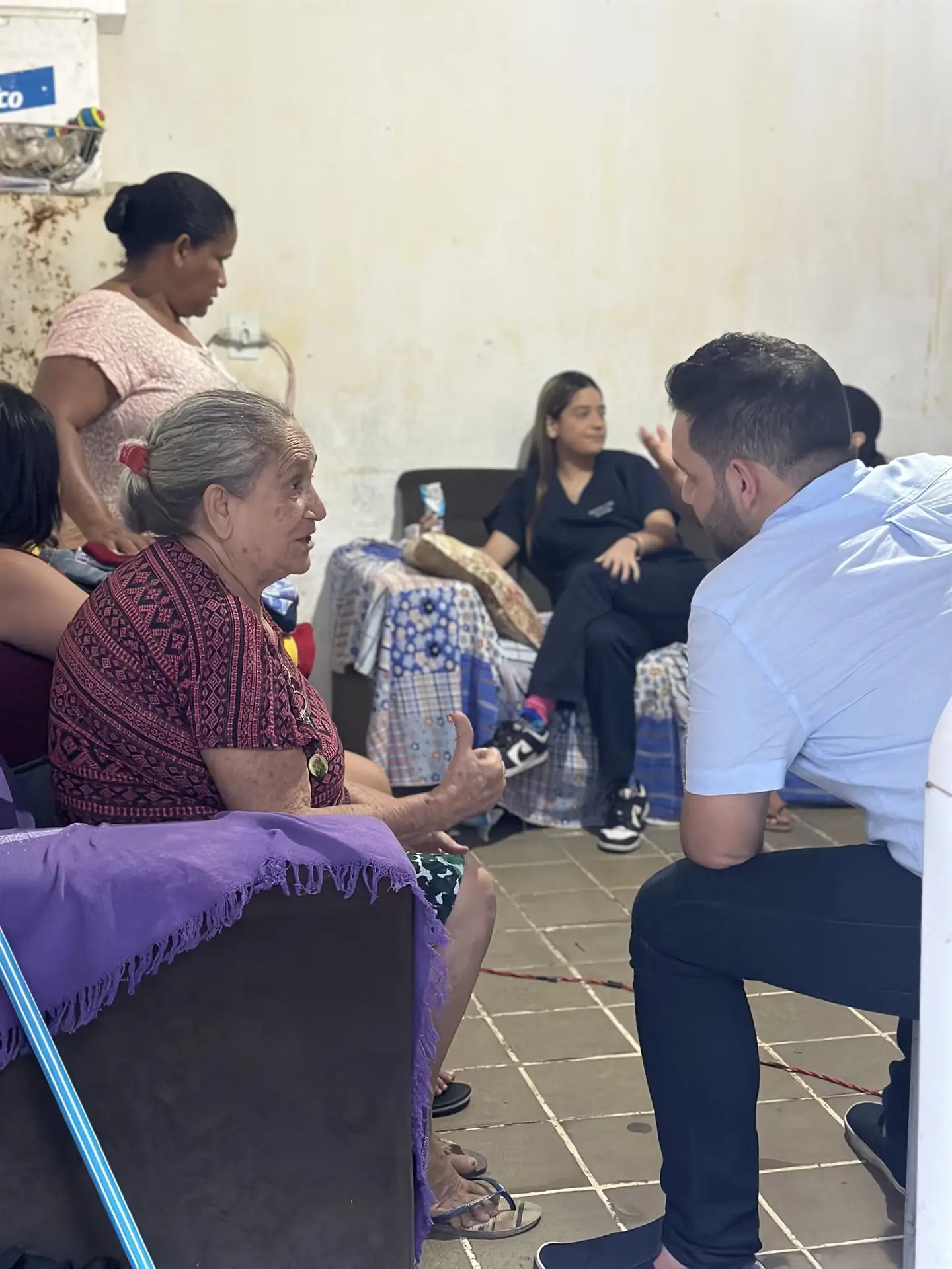 Malory agachado conversa com moradoras dentro de casa